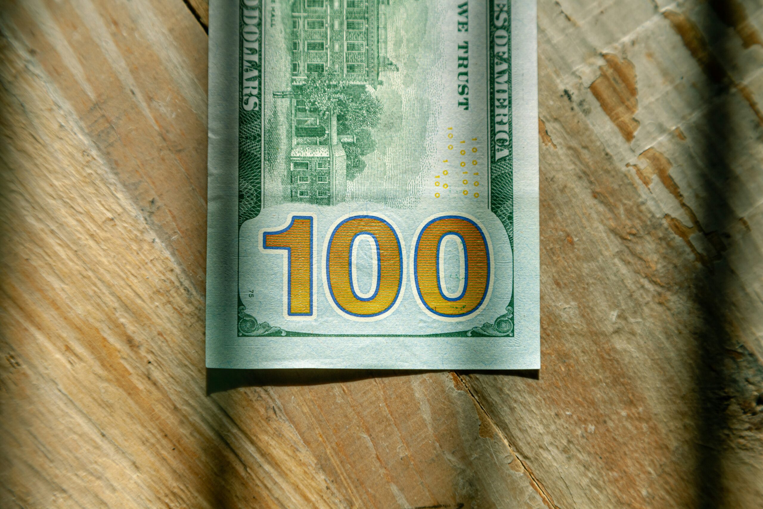 A close-up of the bottom portion of a U.S. one hundred dollar bill placed on a wooden surface, hinting at financial growth projections like LED ROI 2026.