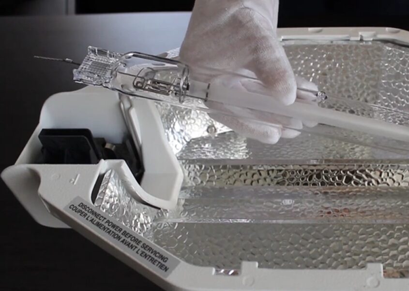 Gloved hands replacing a double-ended HPS lamp in a P.L. Light Systems fixture